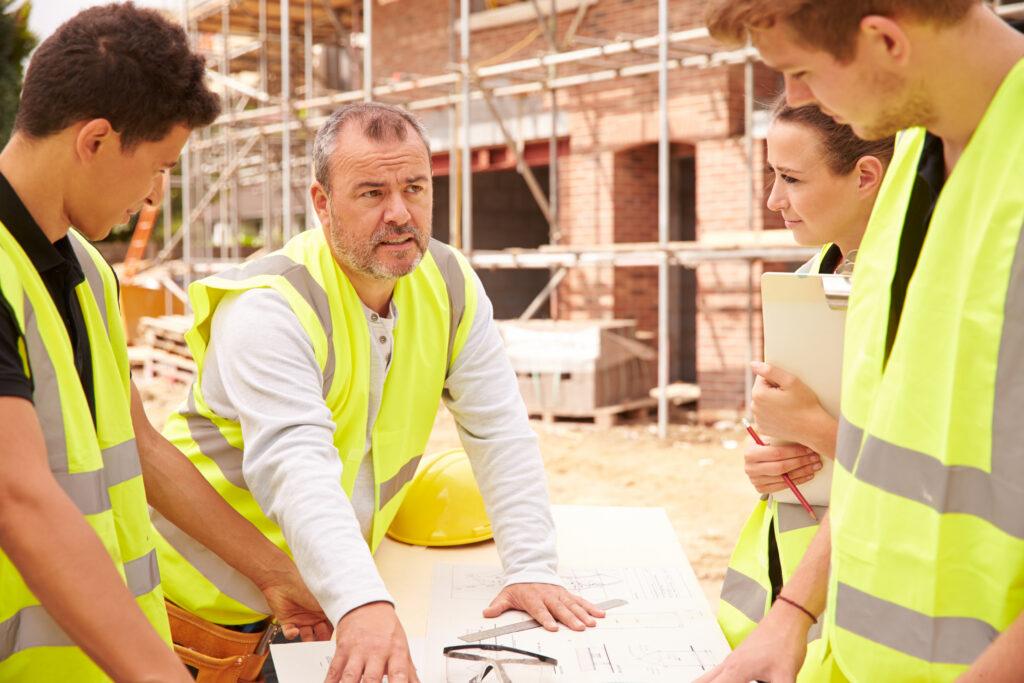 Home Builder On Building Site Discussing Work With Apprentice