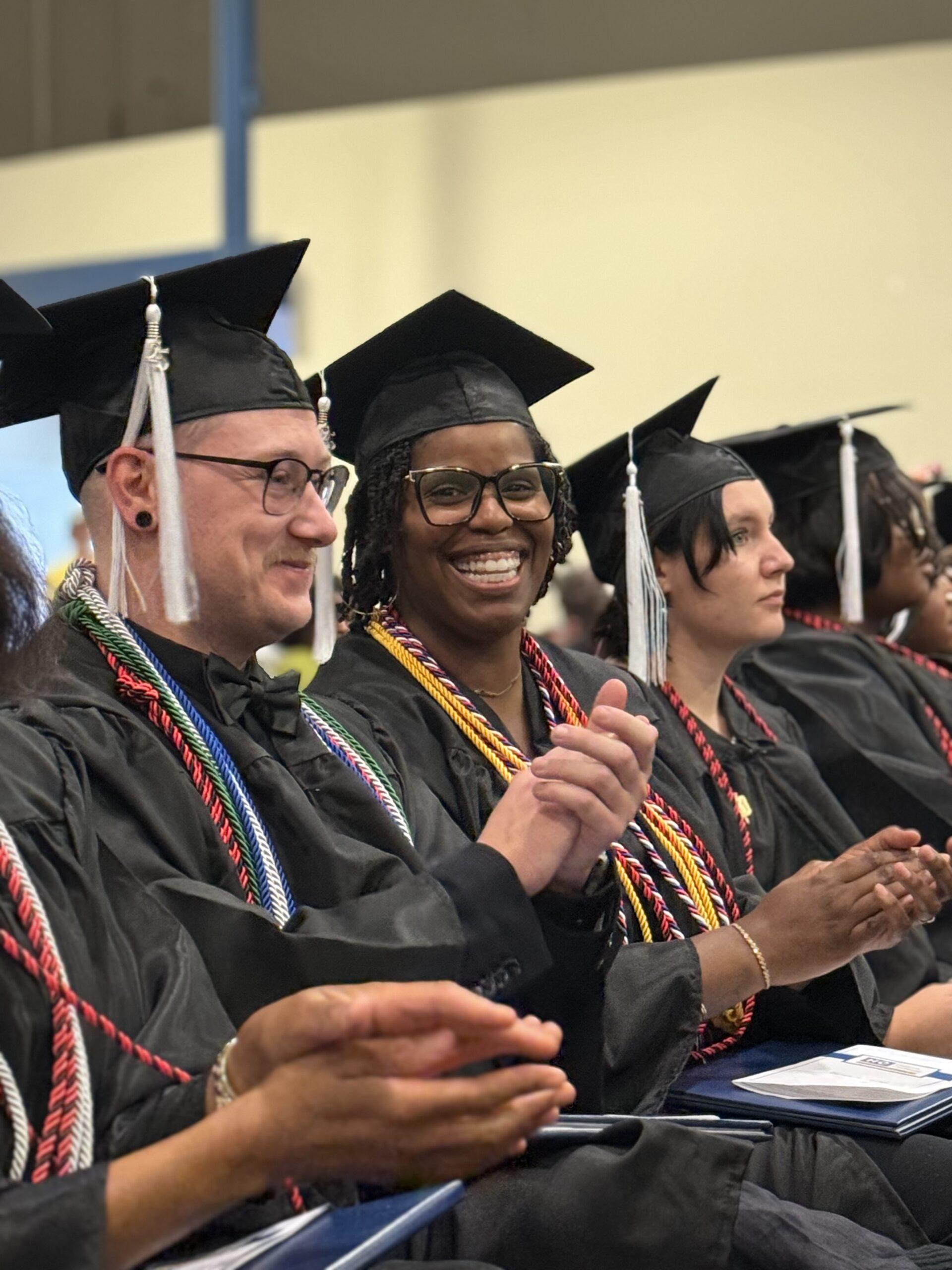 Helms College graduates clap at a ceremony.